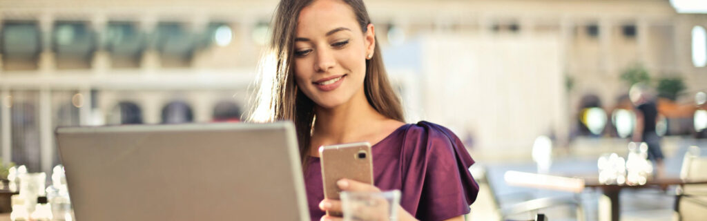 Young woman smiling while using her phone and laptop to find a legal job on Legal Career Connect.